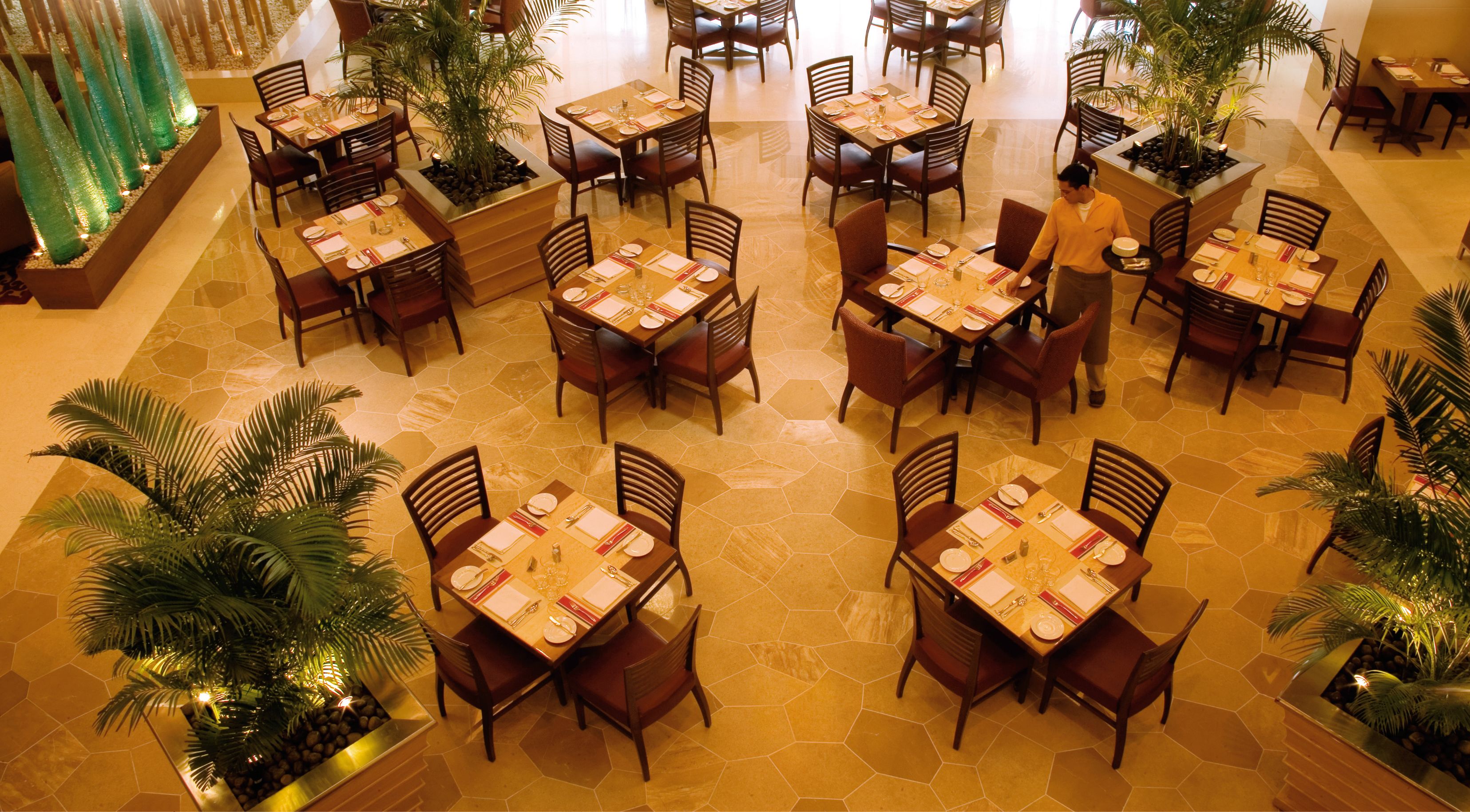 A spacious restaurant with multiple tables and chairs, surrounded by potted plants and decorative elements.