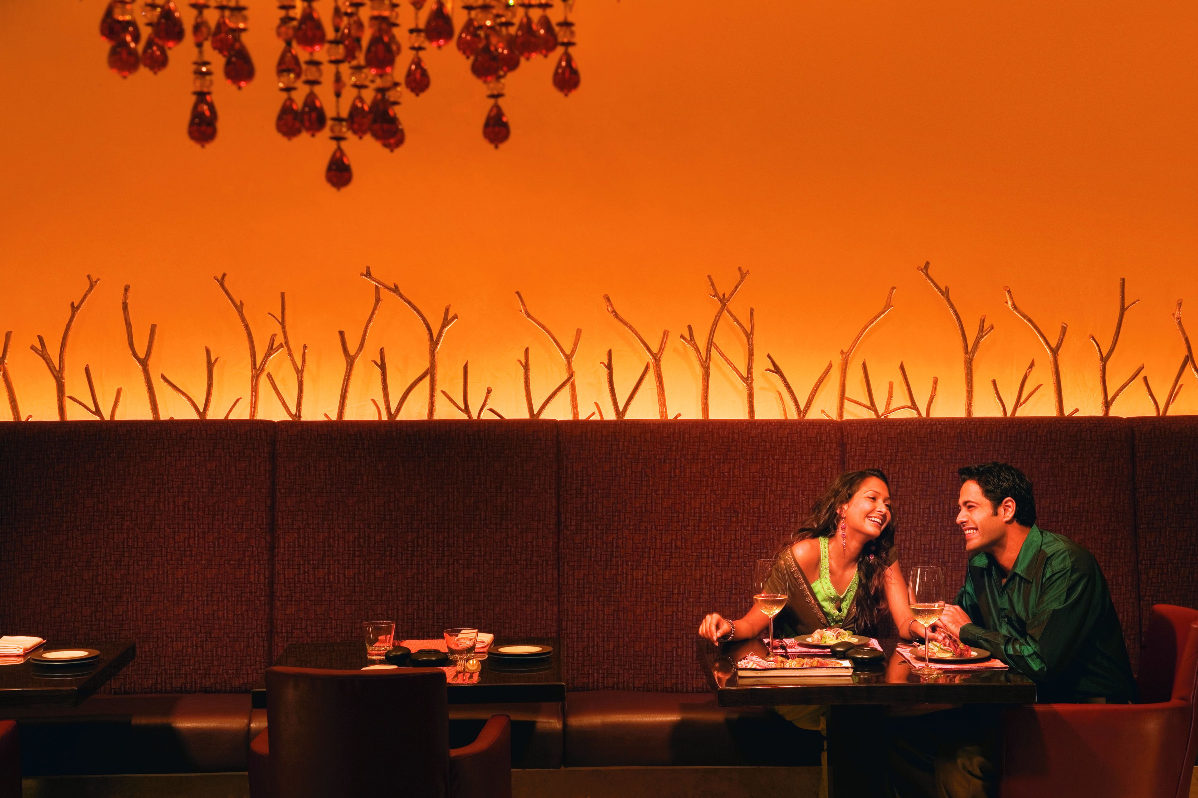 A couple dining in a restaurant with a warm, orange-lit ambiance and a decorative wall with bare branches.