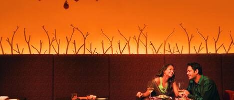 A couple dining in a restaurant with a warm, orange-lit ambiance and a decorative wall with bare branches.