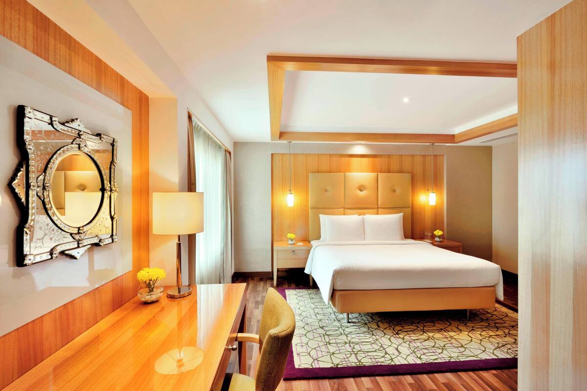 Une chambre d’hôtel avec une tête de lit en bois, un grand miroir, une table de chevet avec une lampe et un lit parfaitement fait.