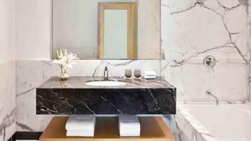 Un baño con lavamanos de mármol, tocador de madera, espejo grande y bañera.