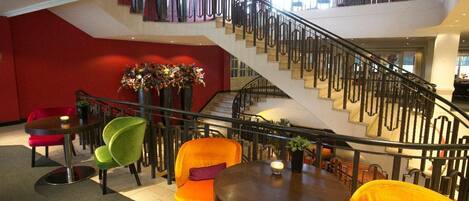 A hotel lobby with a staircase, a round table with a vase, and colorful chairs.