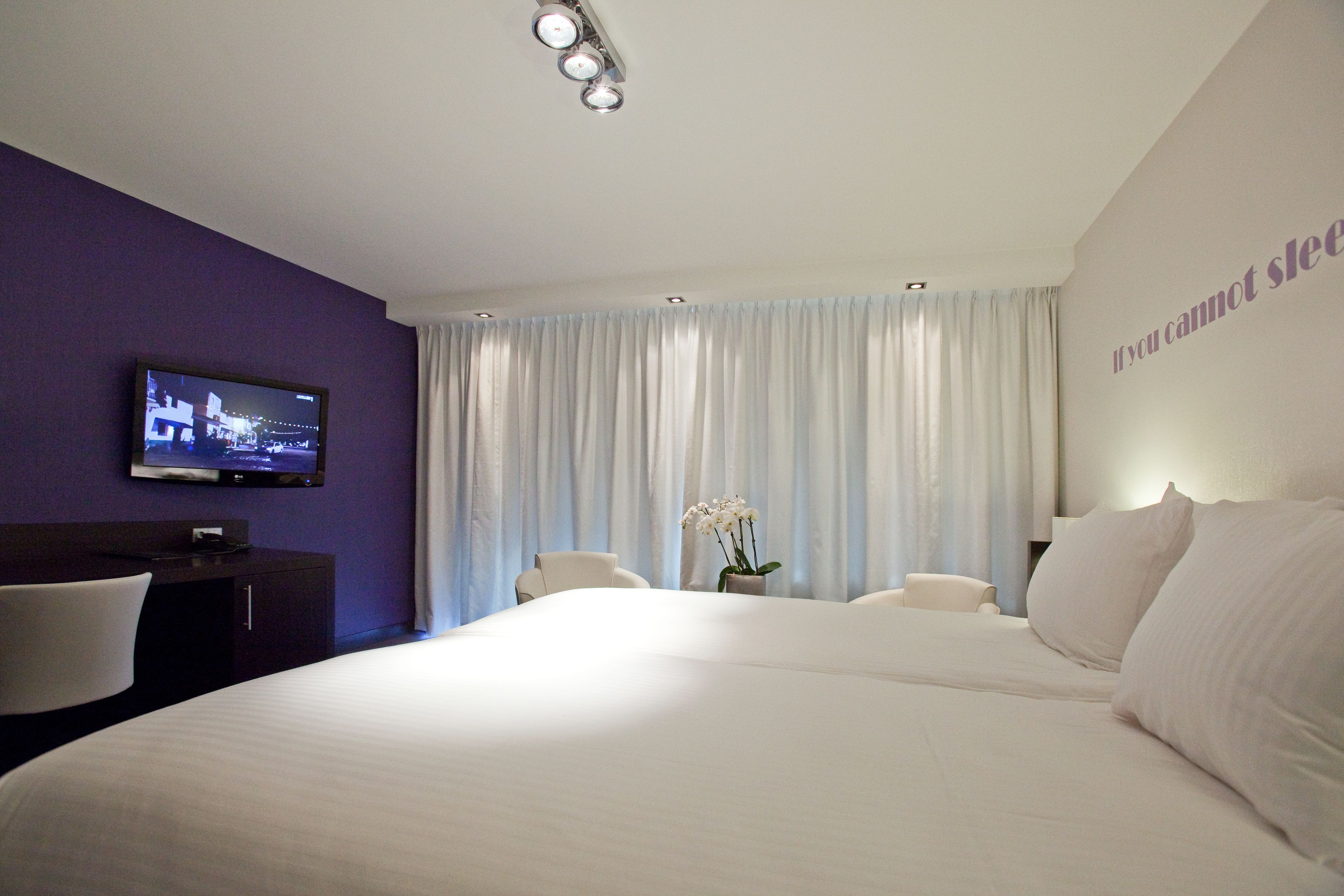 A hotel room with a large bed, a TV mounted on the wall, a desk, and a chair.