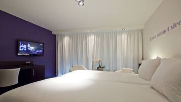 A hotel room with a large bed, a TV mounted on the wall, a desk, and a chair.
