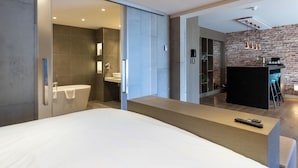 A modern hotel room with a large bed, a bathroom with a bathtub, and a kitchen area with a bar. - Van der Valk Hotel Assen (Assen)