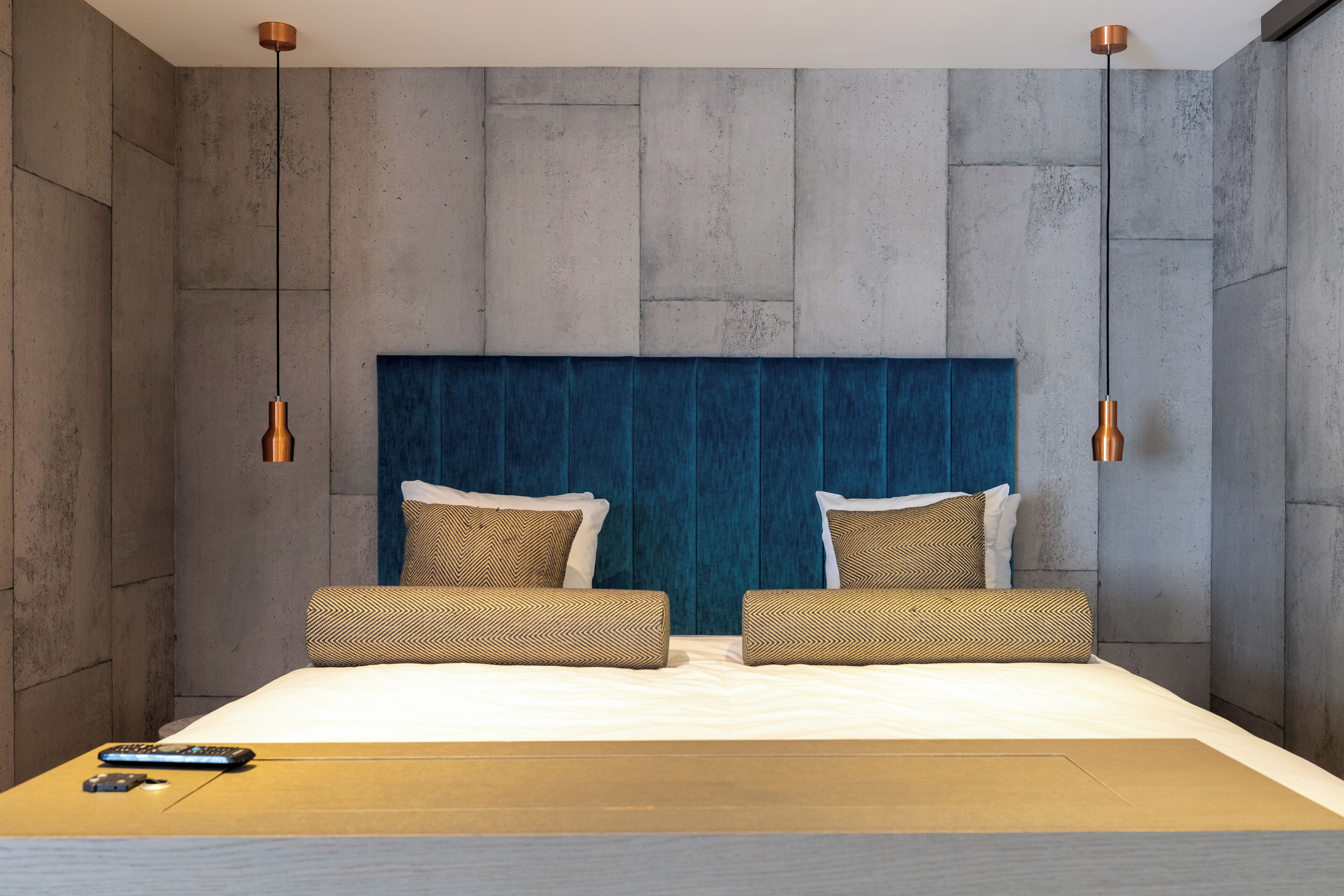 Una habitación de hotel moderna con una cama grande, dos mesitas de noche y un cabecero azul.