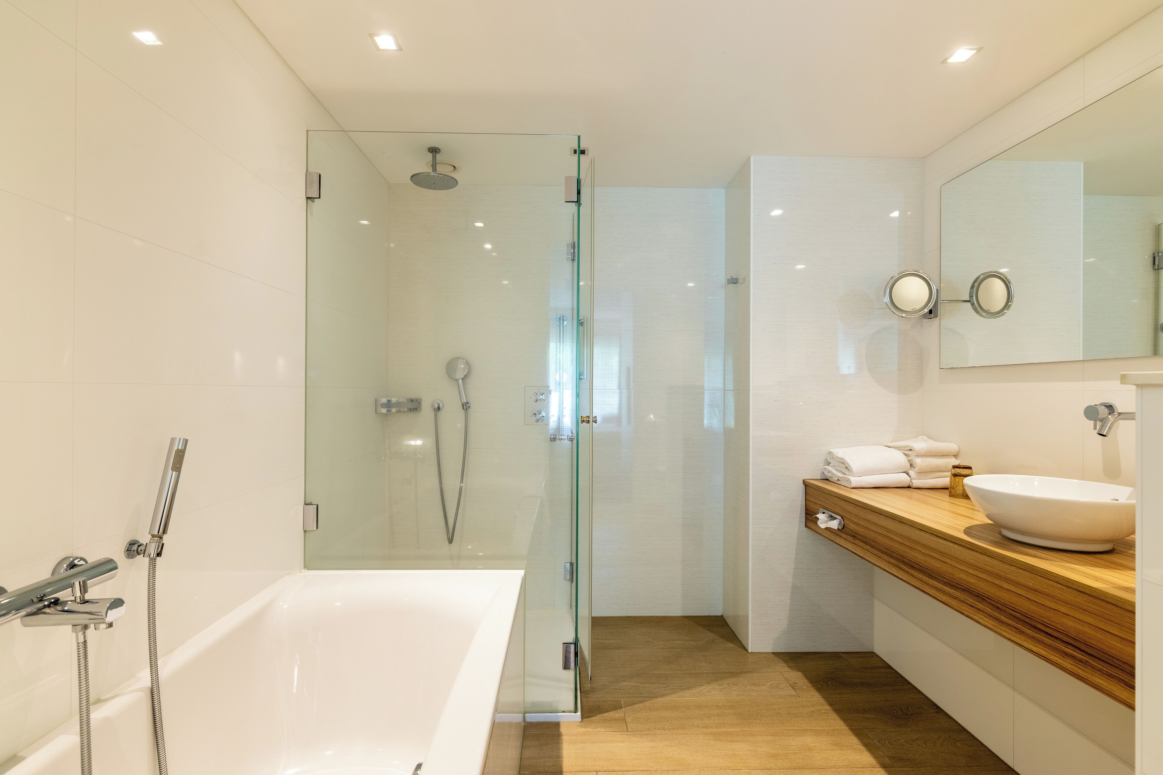 A modern bathroom with a glass-enclosed shower, a white bathtub, and a wooden vanity with a sink.
