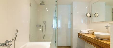Un baño moderno con ducha de vidrio, una bañera blanca y un tocador de madera con lavamanos.