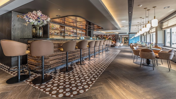 A modern bar area with a long counter, multiple bar stools, and a patterned floor. - Van der Valk Hotel Assen (Assen)