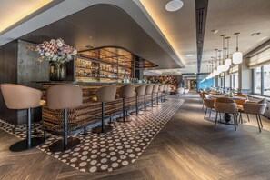A modern bar area with a long counter, multiple bar stools, and a patterned floor. - Van der Valk Hotel Assen (Assen)