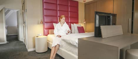 A modern hotel room with a large bed, a built-in wardrobe, a dining area, and a separate bathroom.