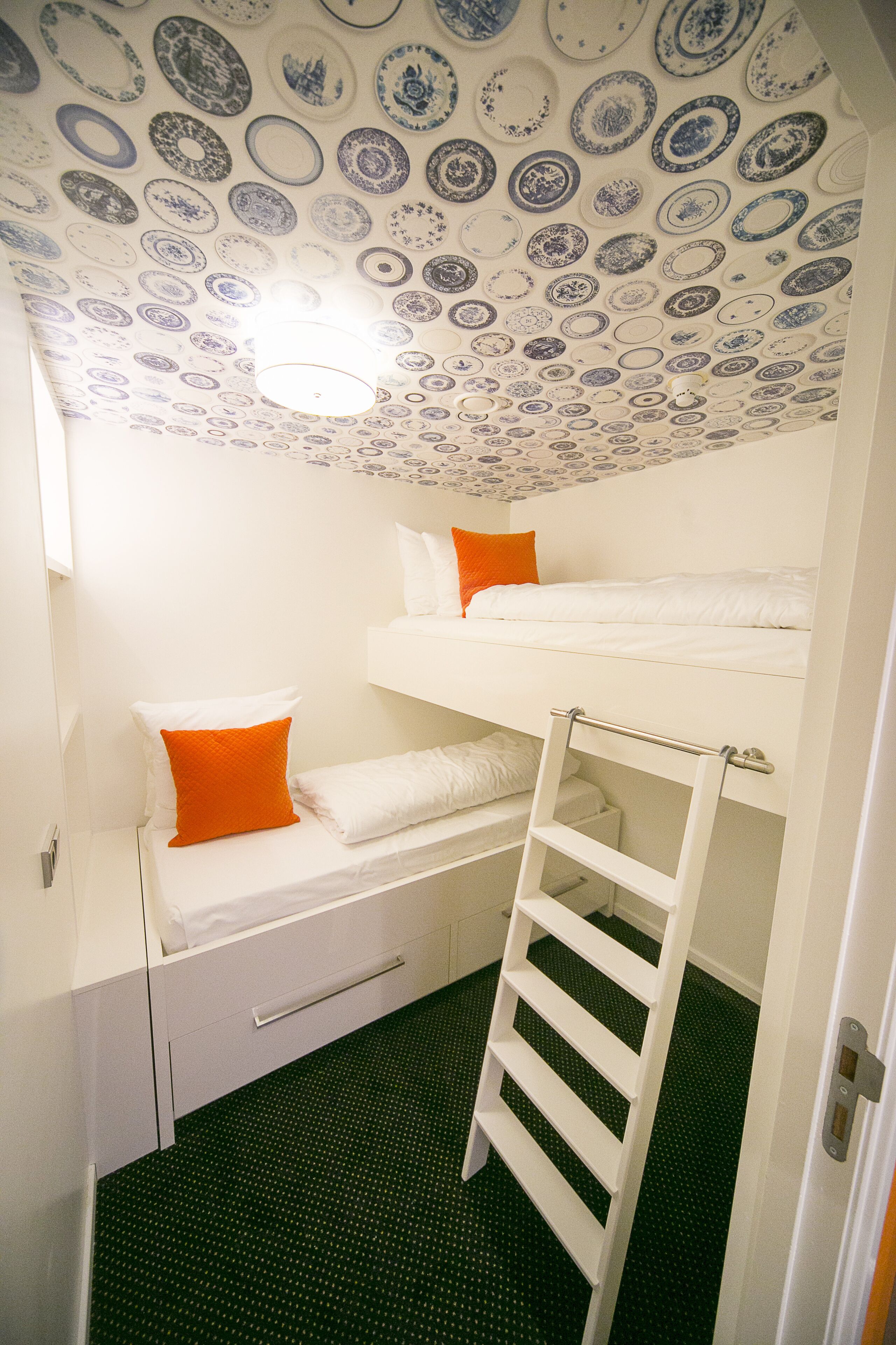 Een slaapkamer met een stapelbed, een enkel bed met een oranje kussen, en een plafond met versierde tegels.