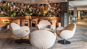 A modern lobby with a seating area featuring round, woven chairs and a wall adorned with tropical plant decorations. - Van der Valk Hotel Assen (Assen)