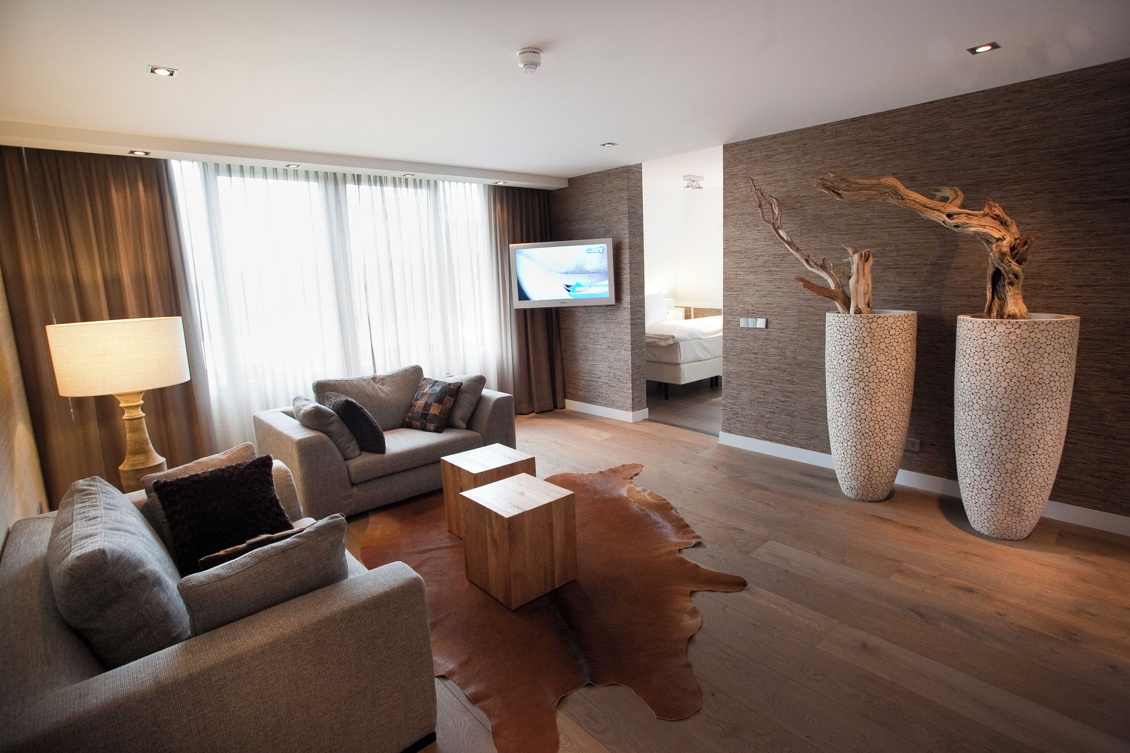 A modern living room with a sofa, coffee table, and a TV mounted on the wall. There are two large vases on the floor and a wooden floor.