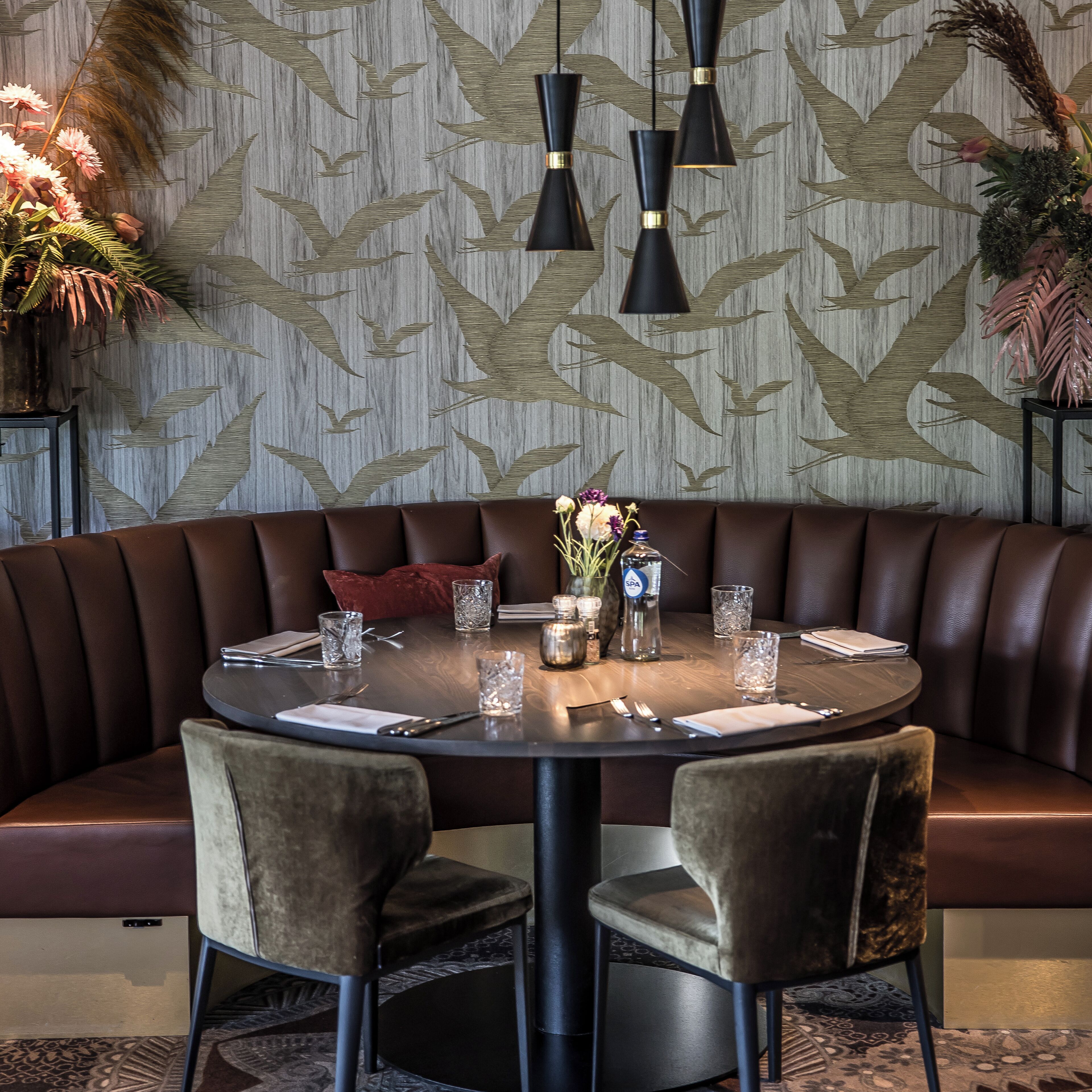 A round dining table with a brown leather booth seating, surrounded by two velvet chairs.