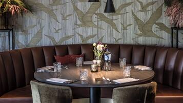 A round dining table with a brown leather booth seating, surrounded by two velvet chairs.