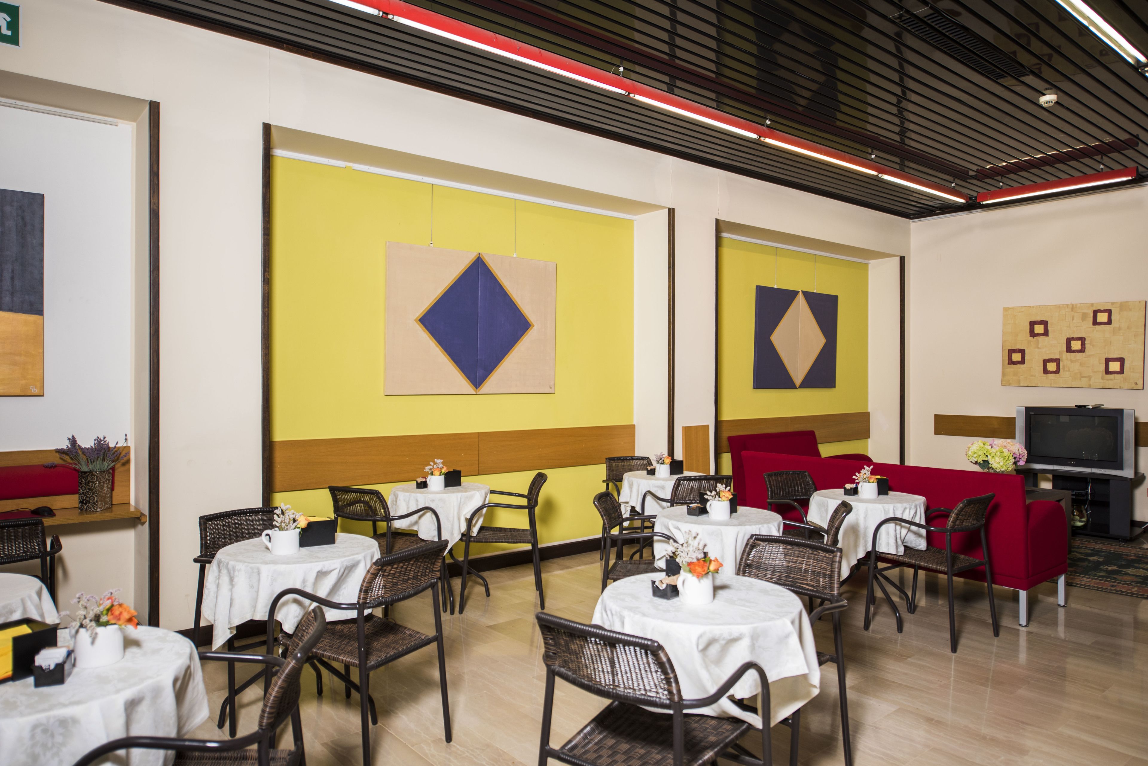 Un espace repas avec des tables rondes, des chaises en osier et des murs aux couleurs jaune et rouge.