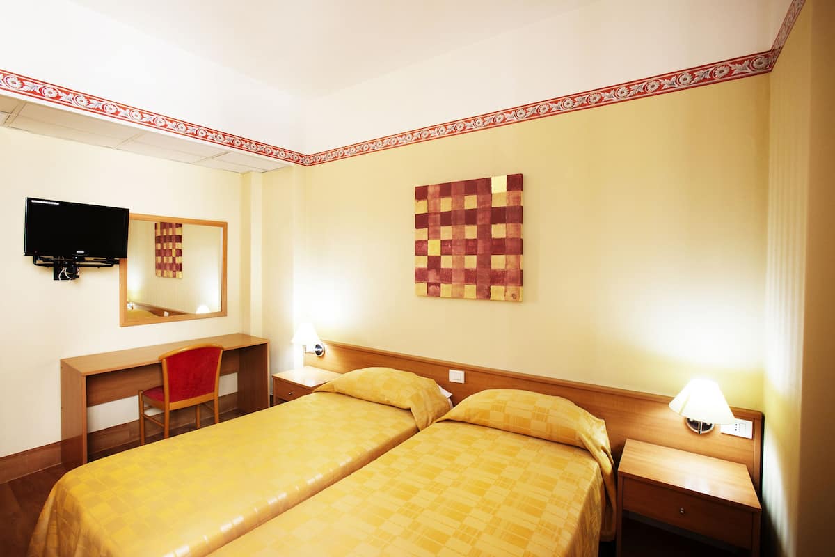 A hotel room with two beds, a desk, a chair, a television, and a wall art piece.