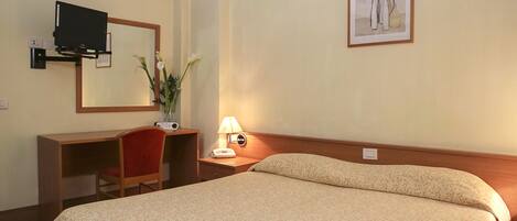 Una habitación de hotel con una cama, un escritorio, una silla, una lámpara, un espejo y un cuadro en la pared.