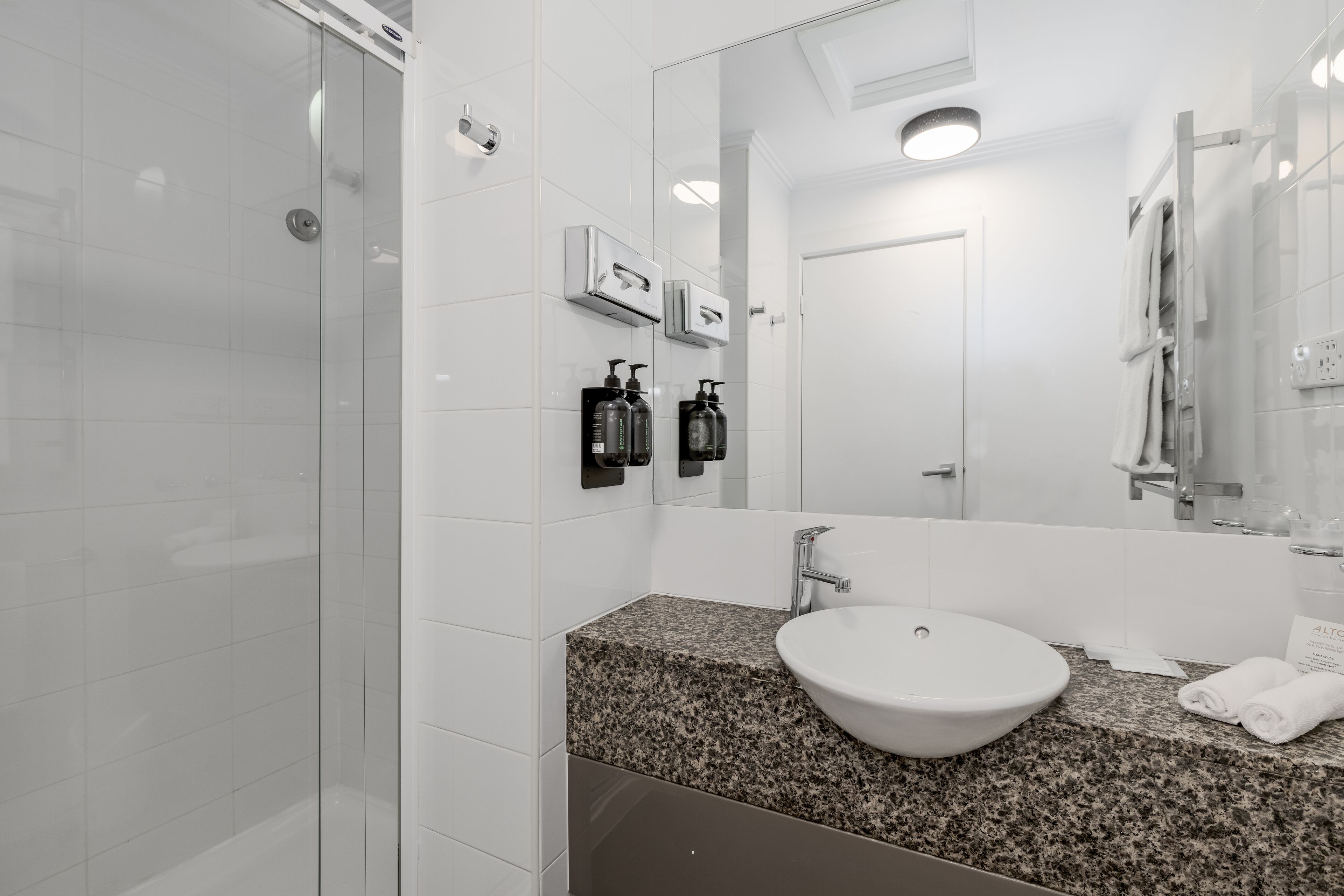 A modern bathroom with a granite countertop, a white sink, and a large mirror.