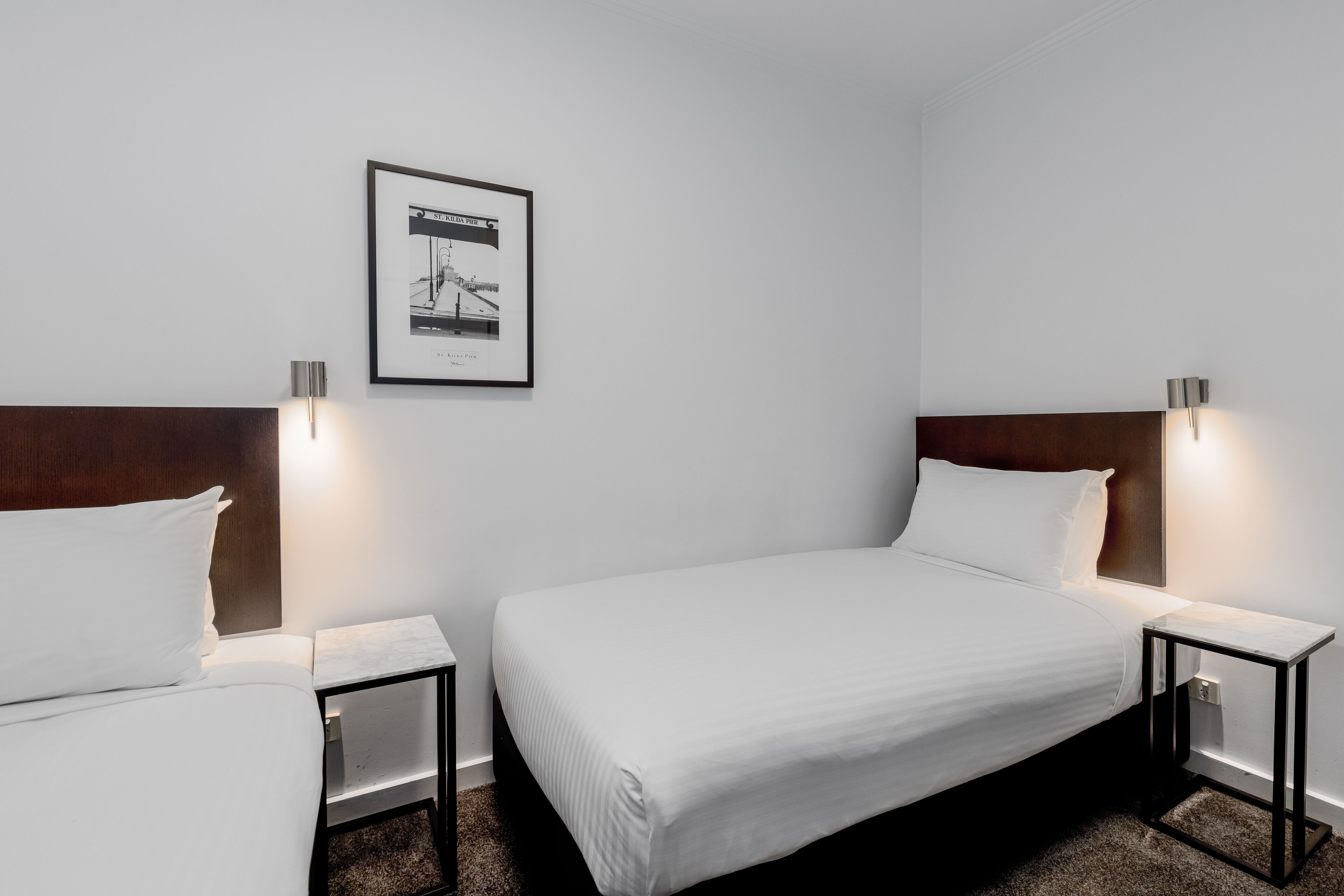 Hotellihuone, jossa on kaksi erillistä sänkyä, seinällä kehystetty taulu ja yöpöydällä lamput.