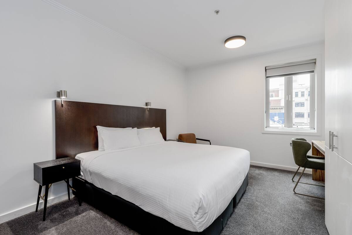 A hotel room with a large bed, a desk, and a chair.