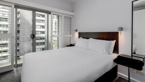 Una habitación de hotel moderna con una cama grande, una mesita de noche, un espejo y una puerta corrediza de vidrio que da a un balcón exterior.