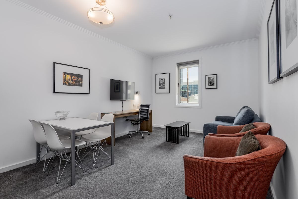 A modern room with a dining table, chairs, a desk, a TV, and a sofa.