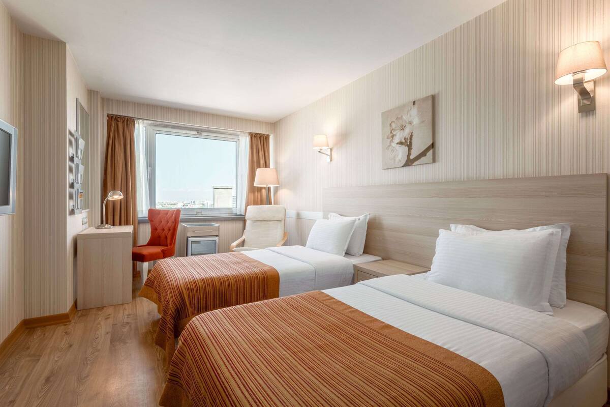 Habitación de hotel con dos camas, un escritorio, una silla y una ventana con cortinas.