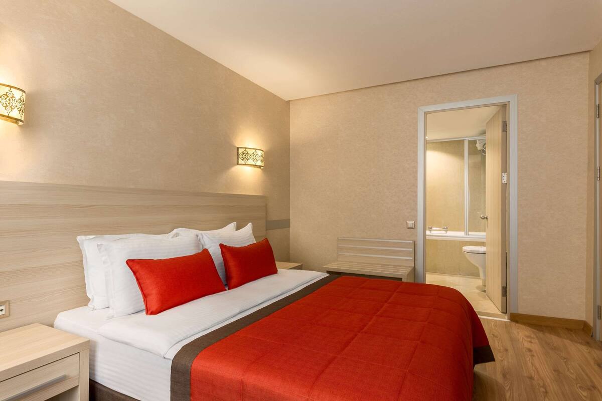 Una habitación de hotel con cama, mesita de noche y apliques de pared.