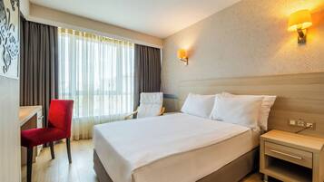 A hotel room with a large bed, a desk with a chair, a nightstand, and a wall-mounted lamp.