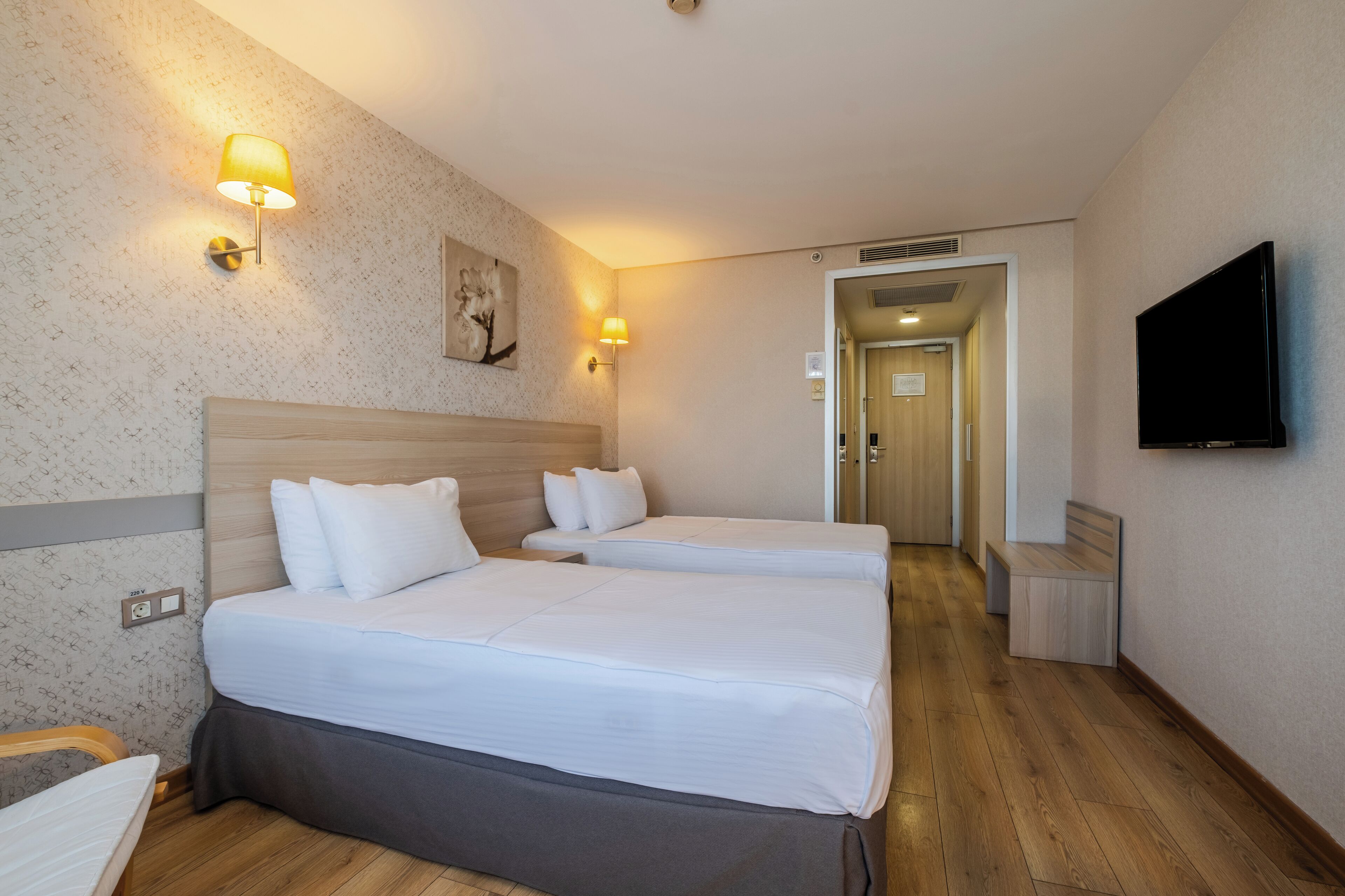 Habitación de hotel con dos camas, un televisor y un pasillo que conduce a otra habitación.