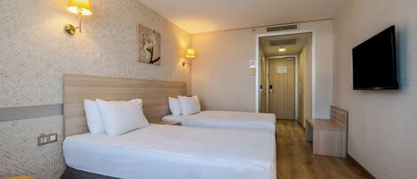 Habitación de hotel con dos camas, un televisor y un pasillo que conduce a otra habitación.