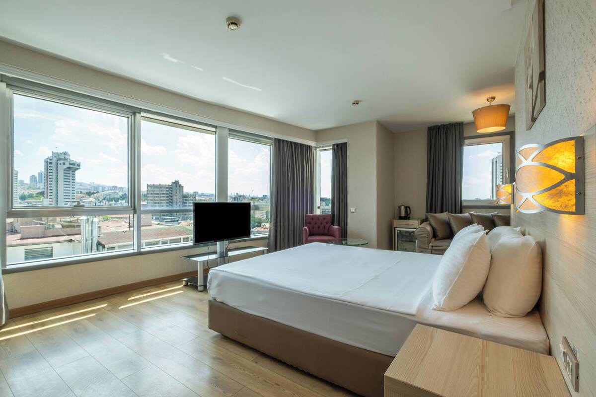 Habitación de hotel con una cama grande, televisión, escritorio y vistas a la ciudad.