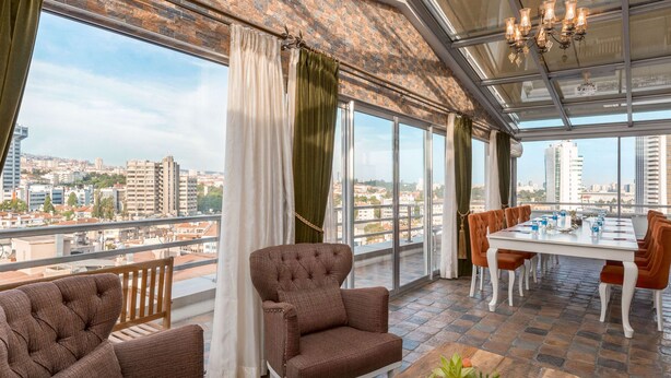 A modern room with a large window, a dining table, and two brown upholstered chairs. - Ramada by Wyndham Ankara (Ankara)