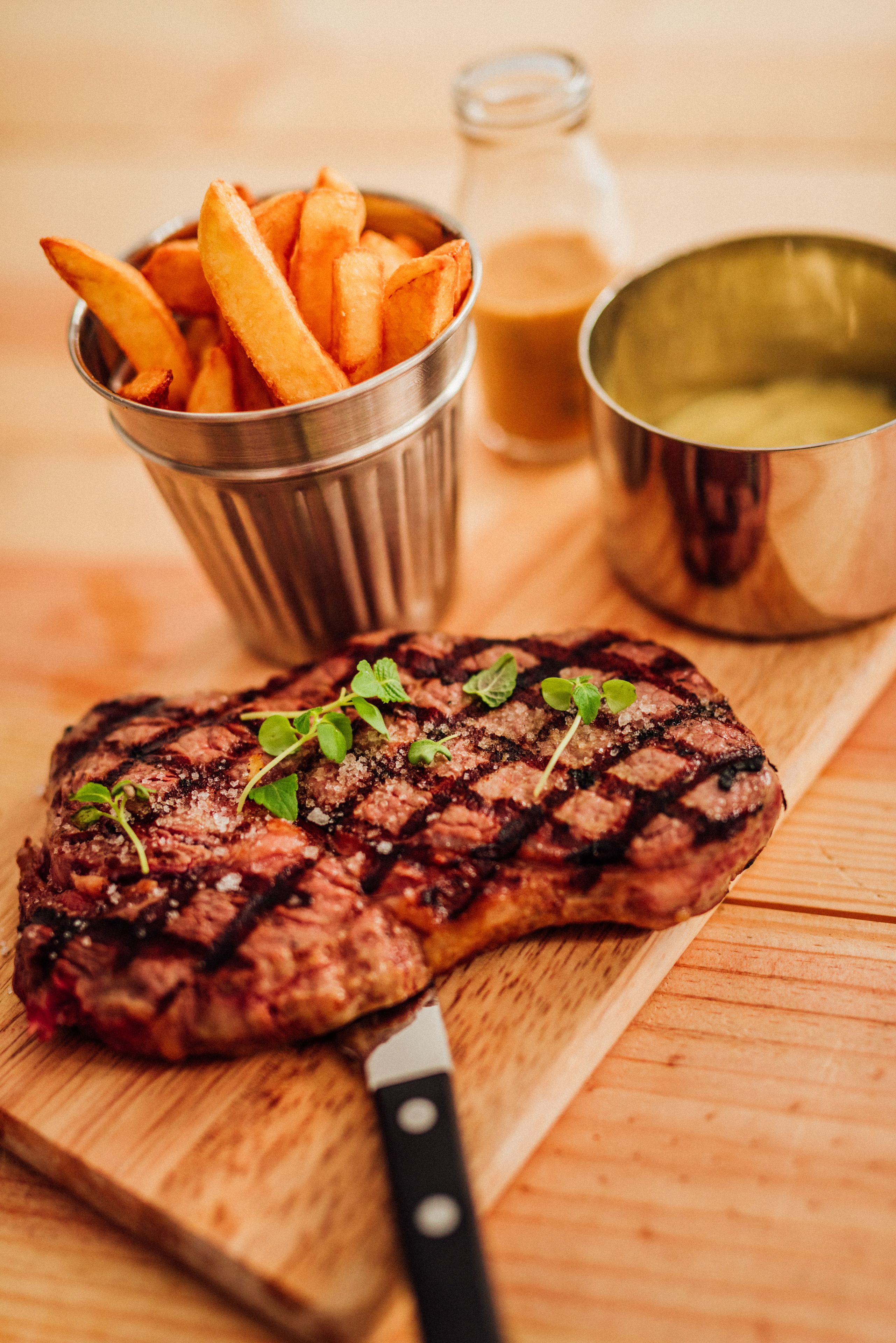 A steak with grill marks and a side of fries on a wooden cutting board.