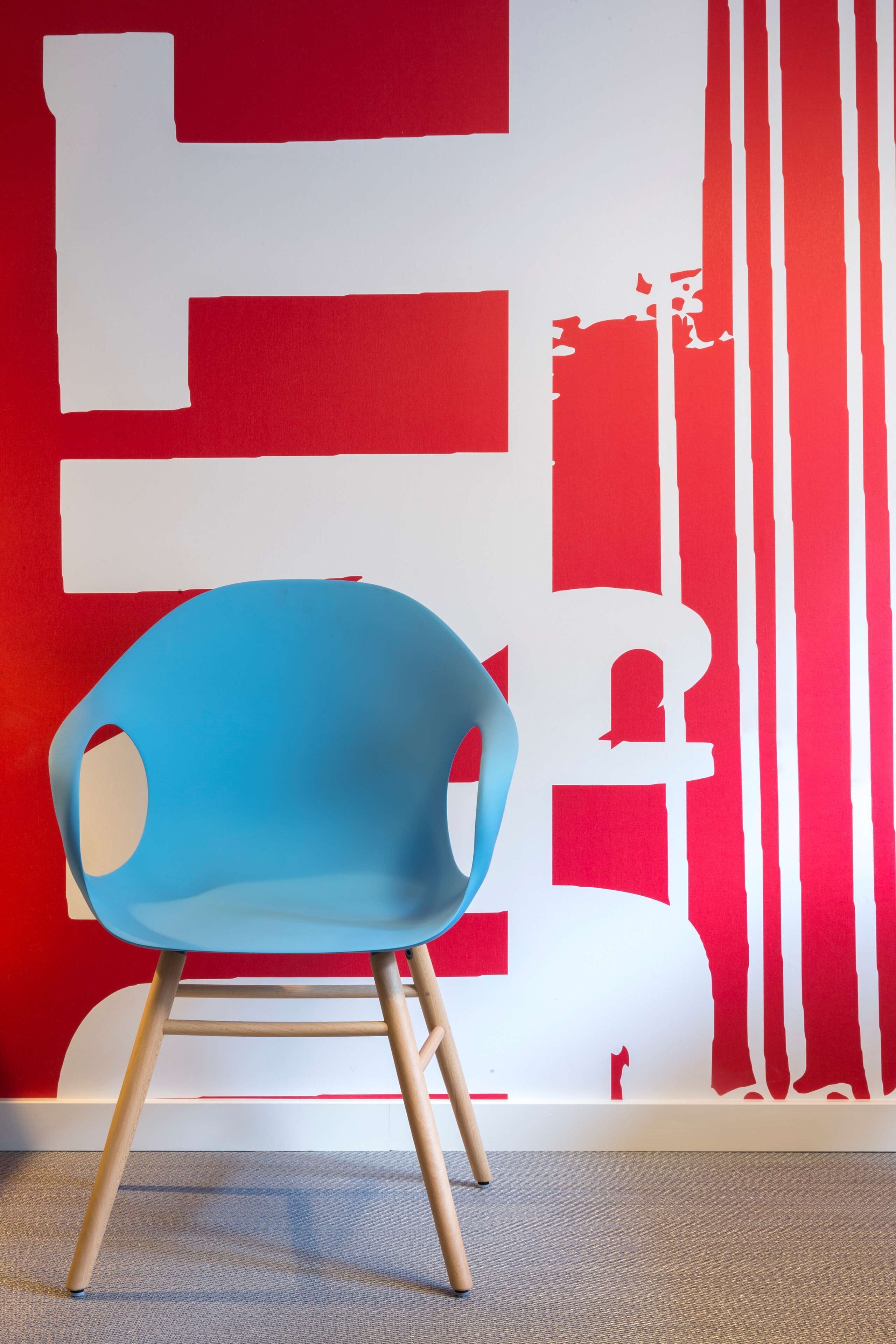 A blue chair with wooden legs in front of a red and white abstract wall.