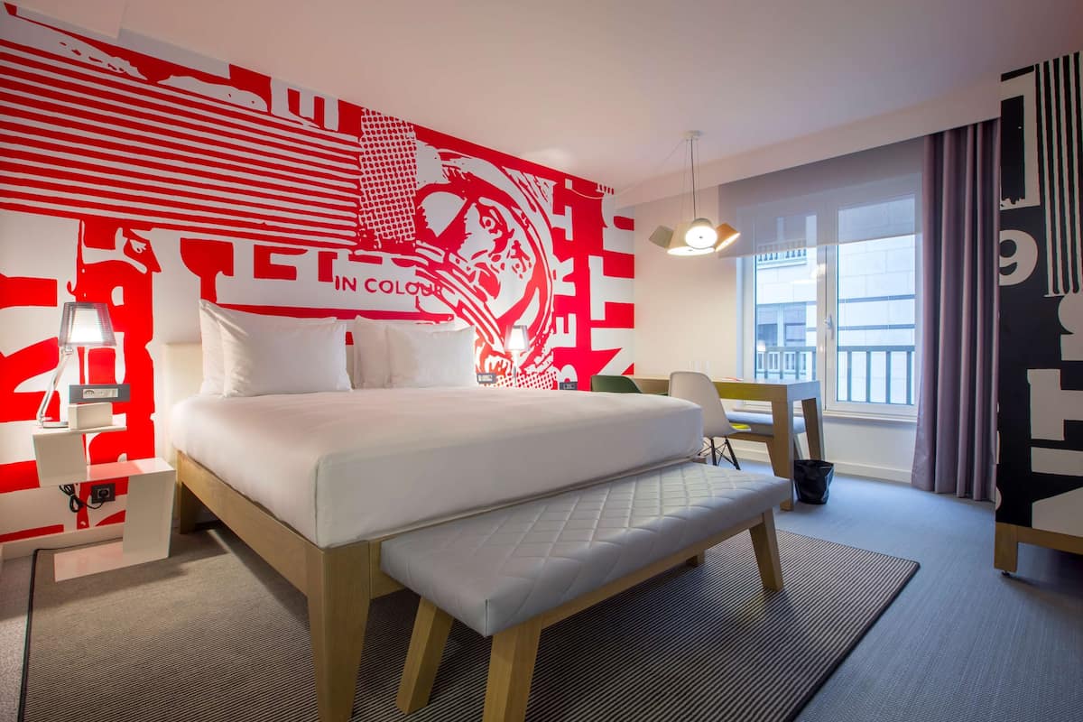 Quarto de hotel moderno com uma cama grande, uma escrivaninha e vista para a cidade.