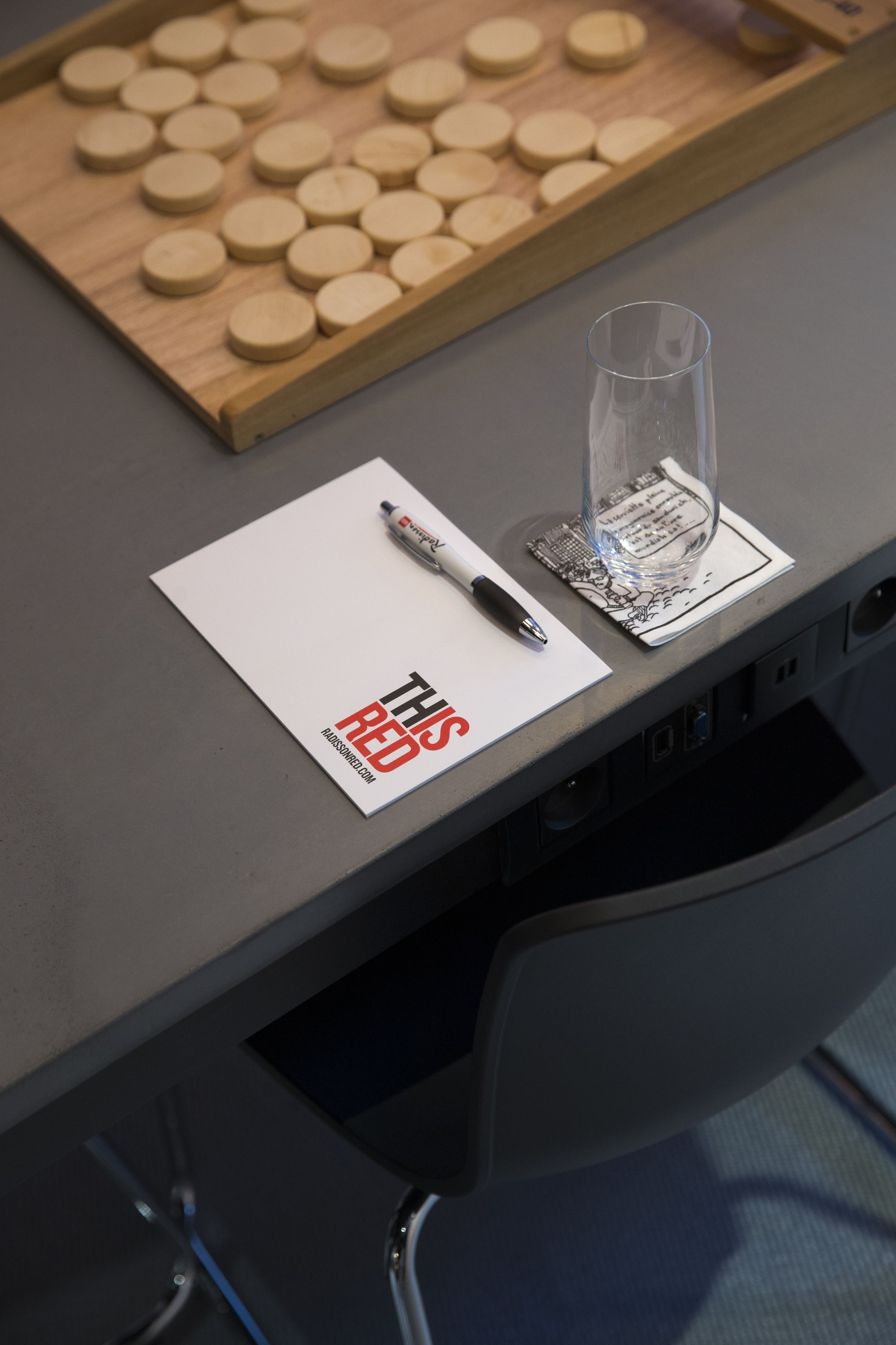 A table with a white placemat, a pen, a glass, and a wooden board game.