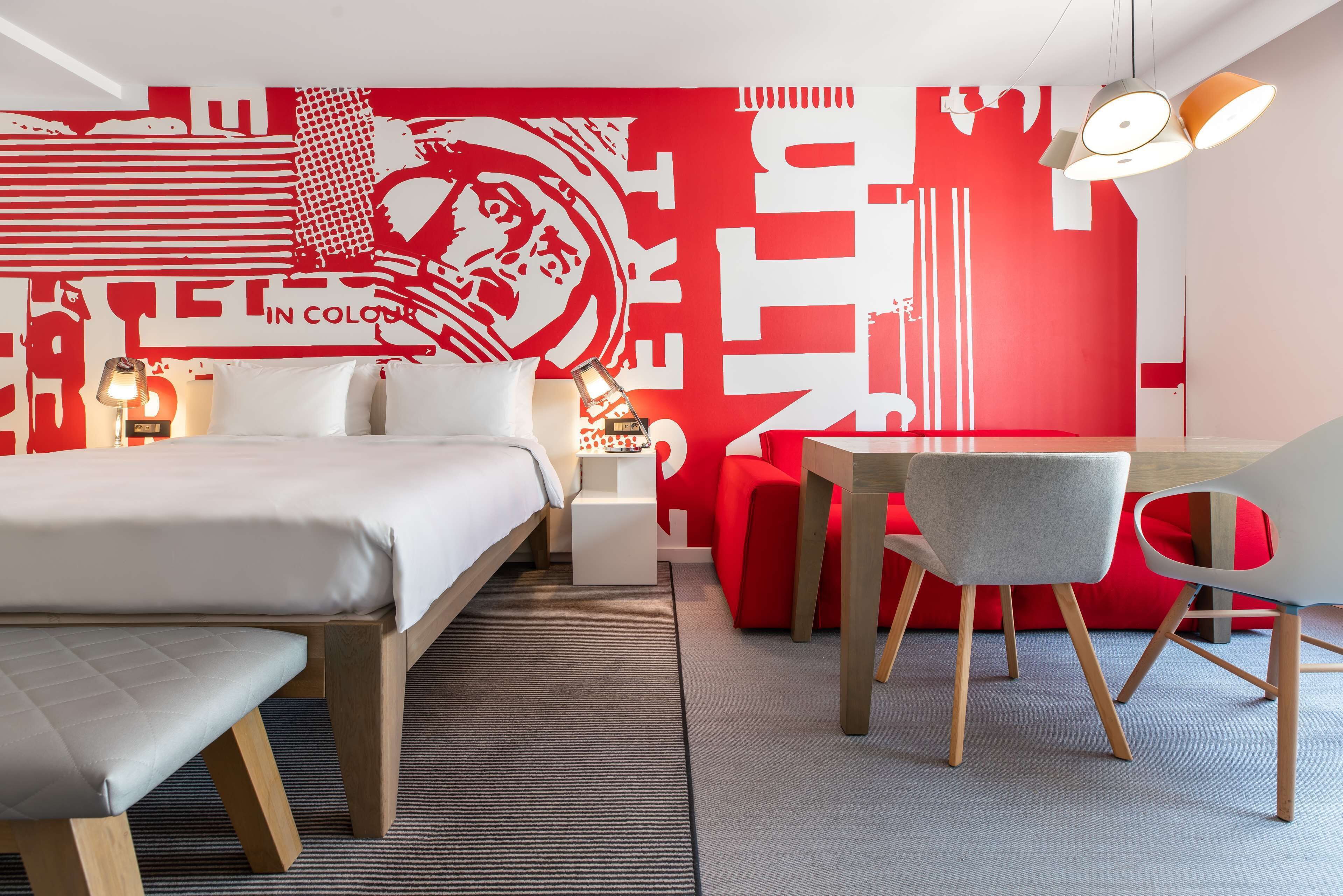 Una habitación de hotel moderna con una cama grande, un escritorio y una pared de acento roja.