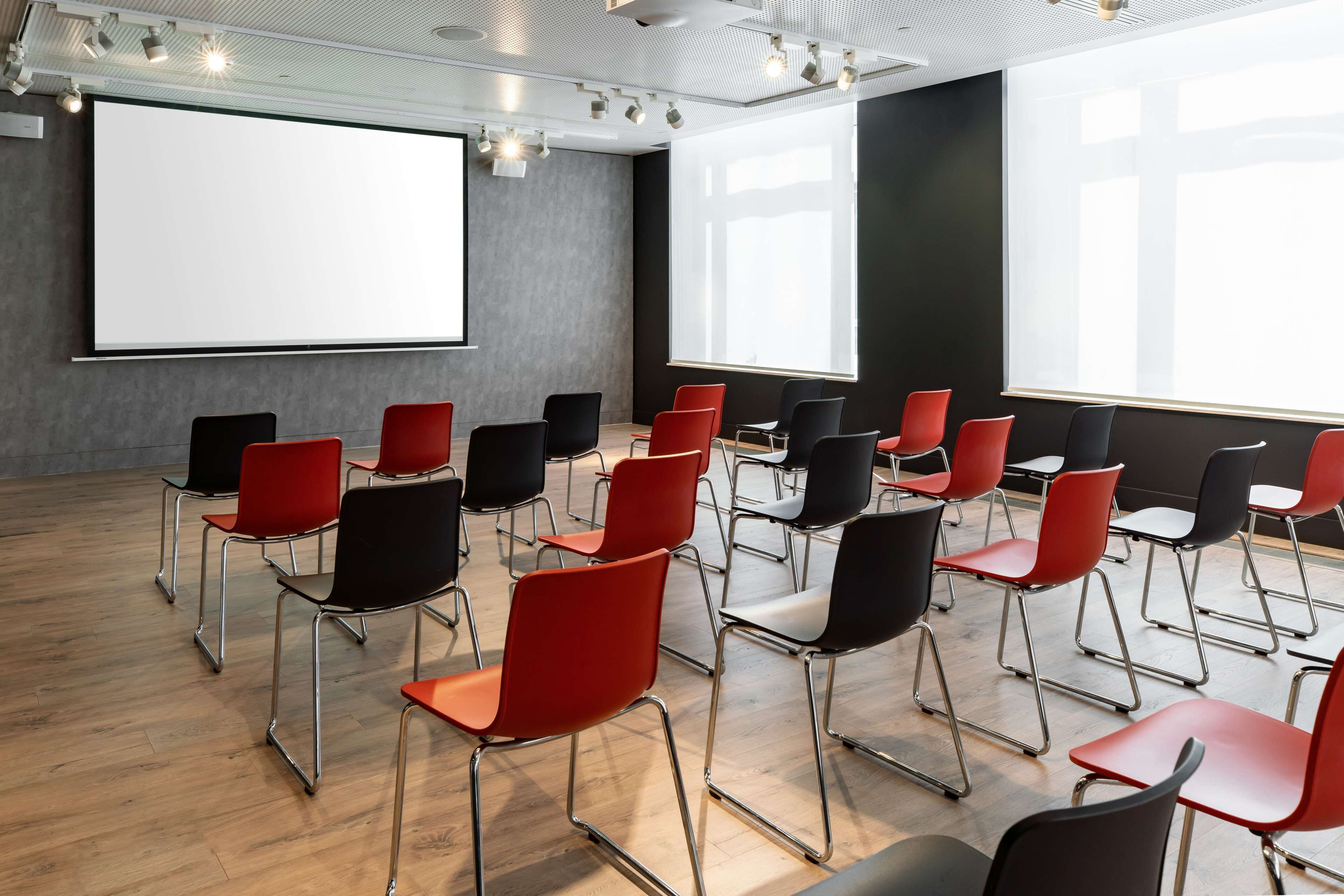A conference room with rows of chairs, a projector screen, and large windows.