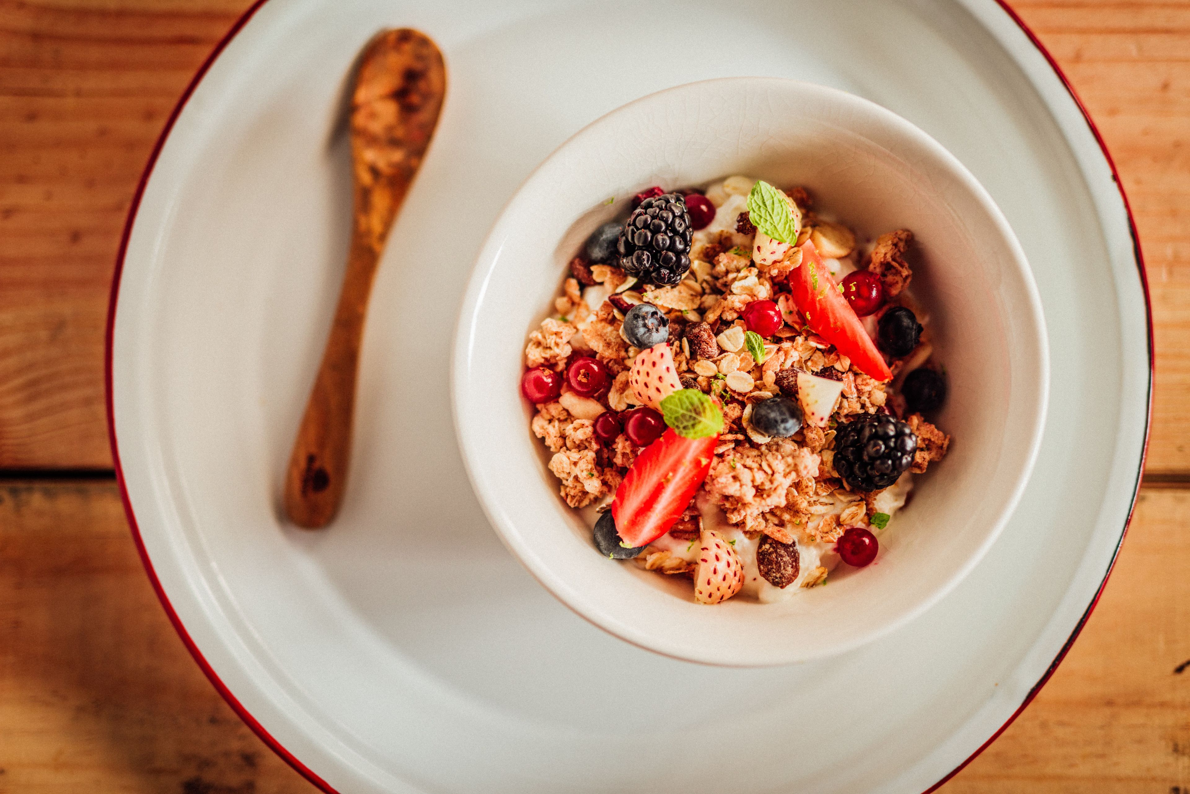 A bowl of cereal with fruits and nuts on a white plate with a red rim.