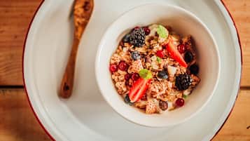 A bowl of cereal with fruits and nuts on a white plate with a red rim.