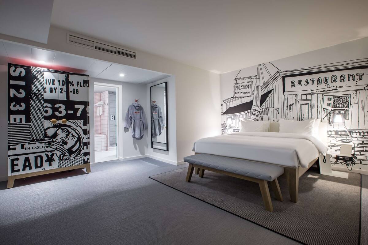 Quarto de hotel moderno com uma cama grande, um banco, um guarda-roupa e um mural na parede.
