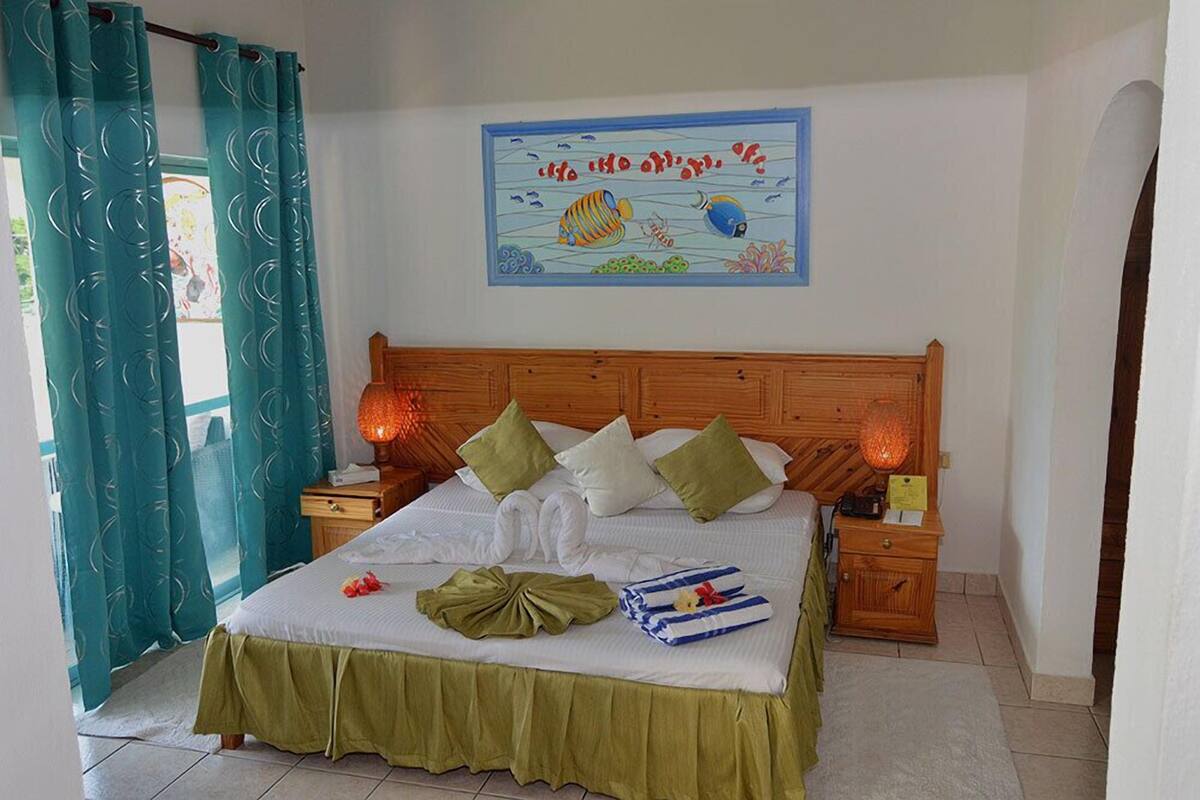 Una cama bien hecha con almohadas, un cabecero y una mesita de noche con una lámpara.