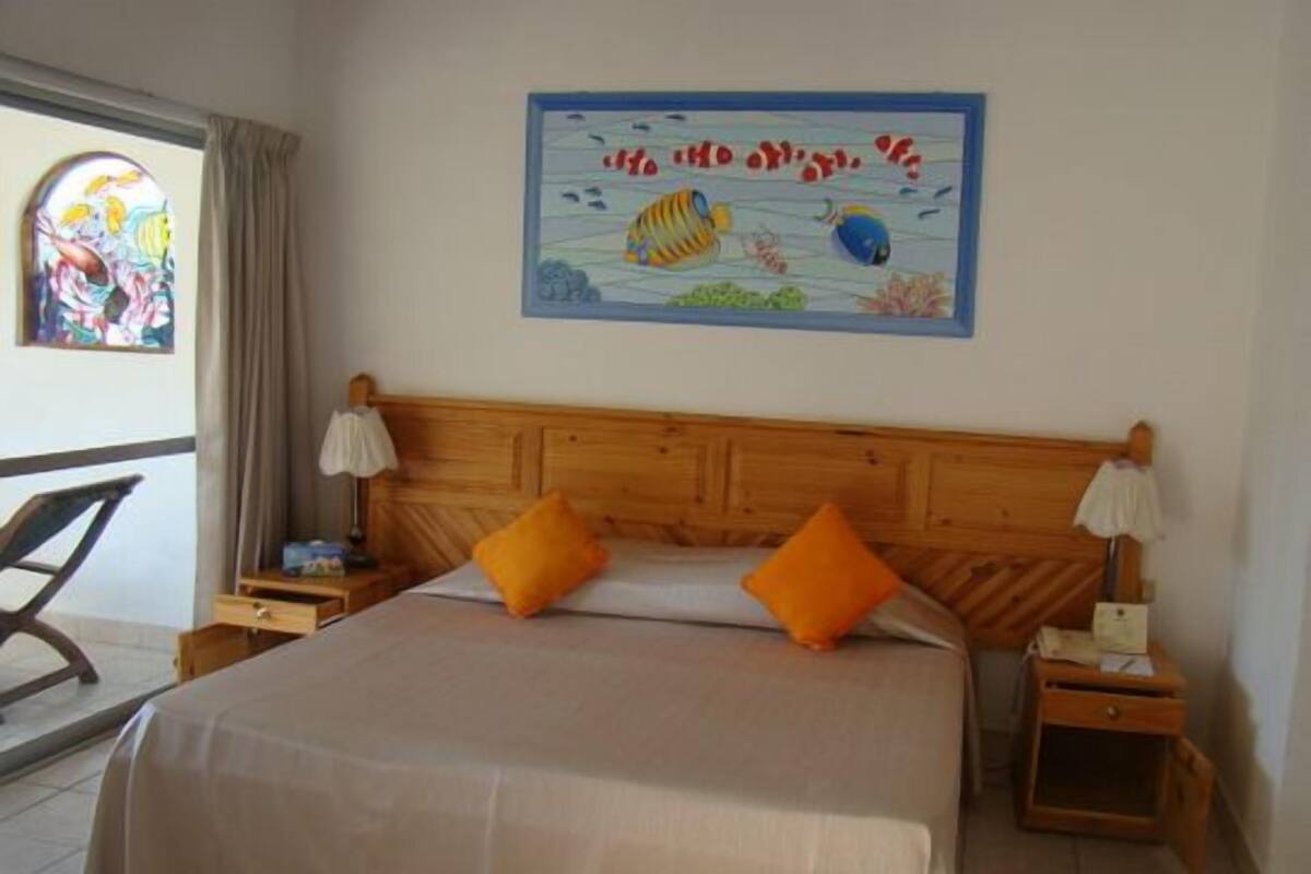 Habitación de hotel con una cama grande, dos mesitas de noche, un cabecero de madera y un cuadro de peces en la pared.