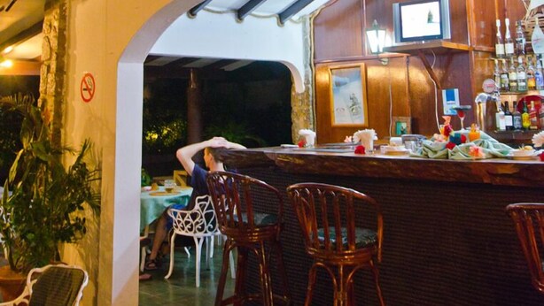 Eine Bar mit Holzsesseln, einem an der Wand befestigten Fernseher und einem Schild mit der Aufschrift 'Coco Hotel'.