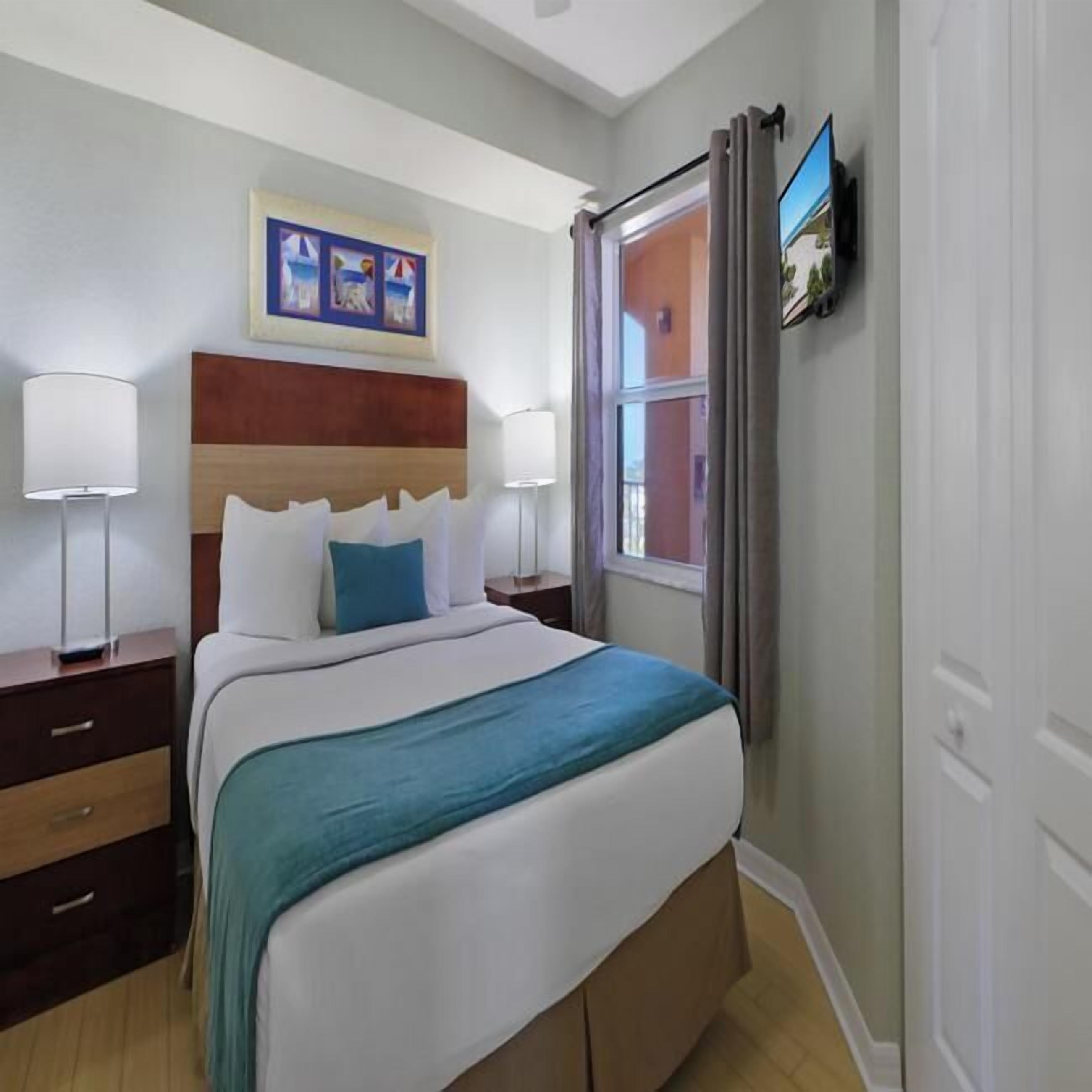 Quarto com cama, mesas de cabeceira, janela com cortinas e um quadro na parede.