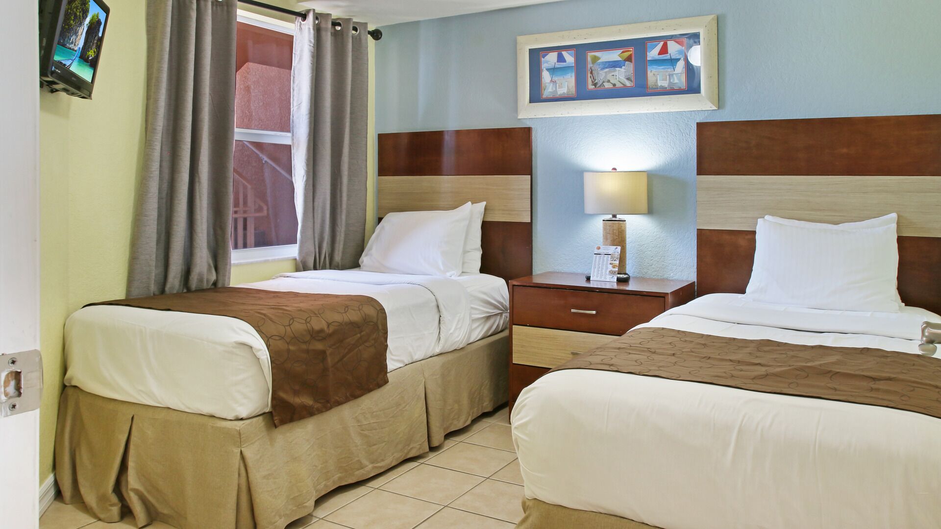 Une chambre d’hôtel avec deux lits, une table de chevet, une lampe et une fenêtre avec des rideaux.