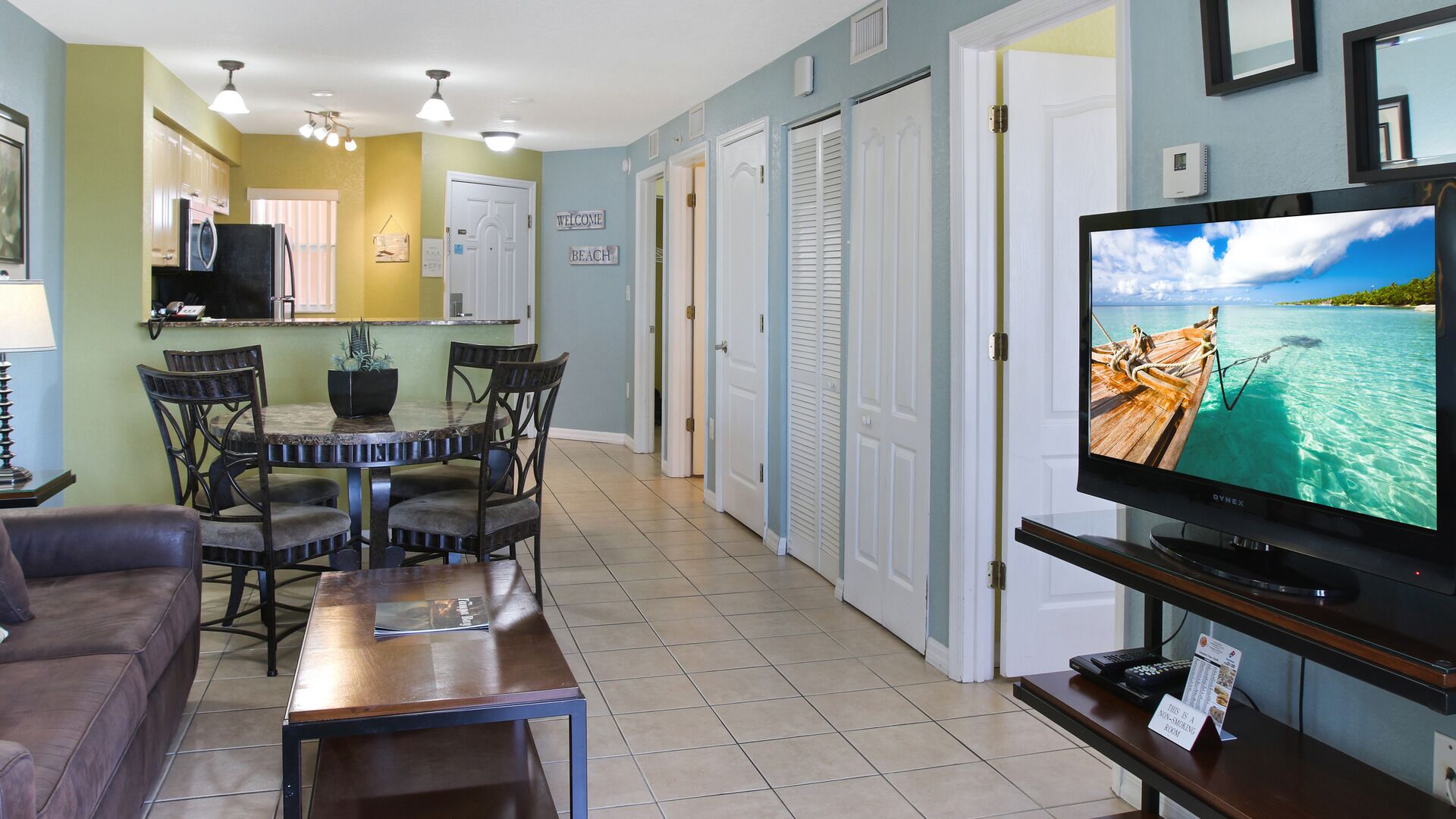 A living room with a dining area, a TV on a stand, and a view of the ocean through the window.